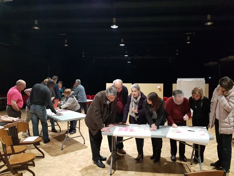 Des participants travaillent en groupes autour de tables couvertes de notes et de propositions.